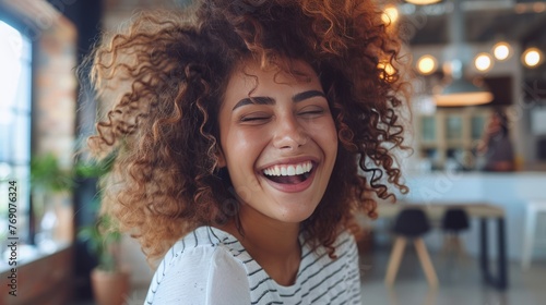 Portrait of beautiful young woman laughing at creative office. Happy businesswoman with curly hair excited with toothy smile. Enthusiastic cheerful girl looking at camera photo