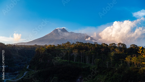 The beauty of Mount Merapi at dusk before dark with a cliff of cold lava flows right in front of it. Mount Merapi looks detailed on a clear day with blue sky and clouds beside it © Yasuspade