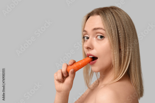 Young woman eating carrot on light background, closeup