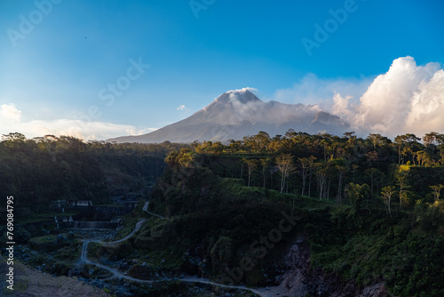 The beauty of Mount Merapi at dusk before dark with a cliff of cold lava flows right in front of it. Mount Merapi looks detailed on a clear day with blue sky and clouds beside it