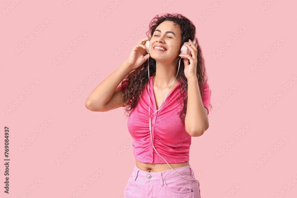 Young African-American woman with headphones listening to music on pink background - obrazy, fototapety, plakaty 