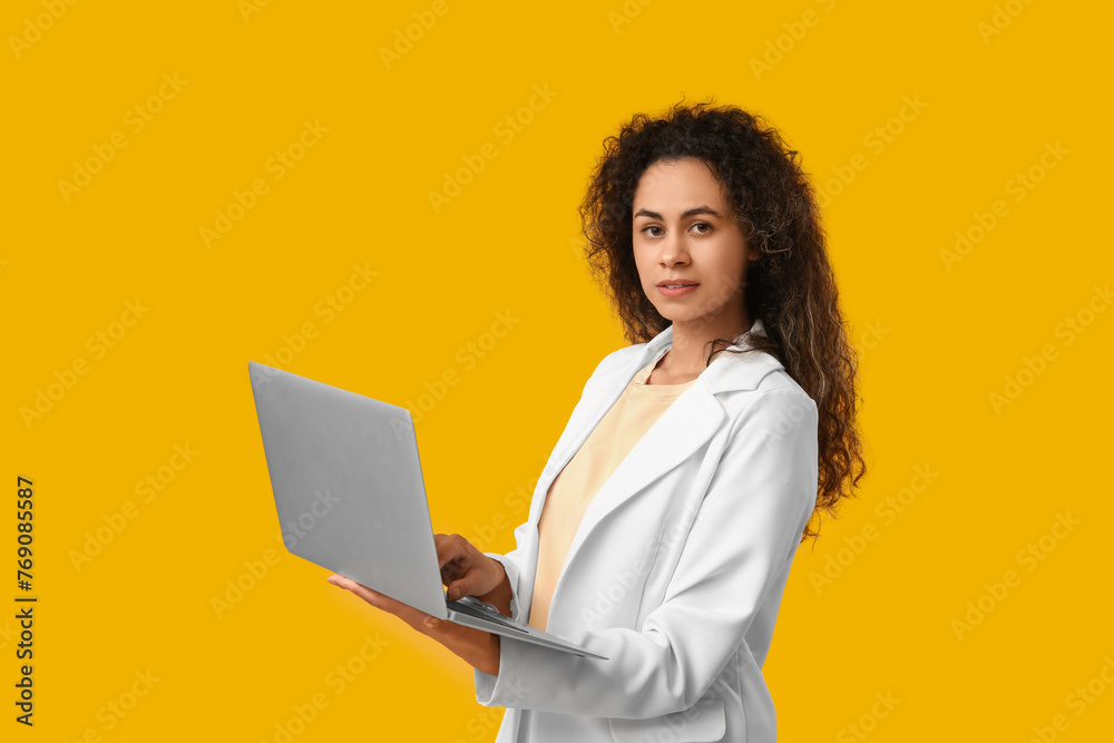 Young African-American businesswoman with modern laptop on yellow background Young African-American businesswoman with modern laptop on yellow background