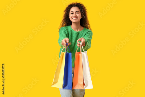 Young African-American woman with shopping bags on yellow background