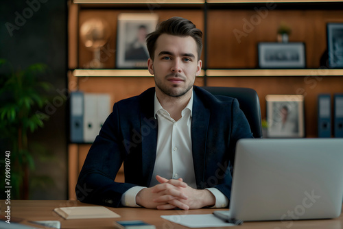 Portrait of confident young man,businessman,executive director, boss,sitting at an office desk with laptop in business suit and looking at camera with his arms crossed,concept of business materials