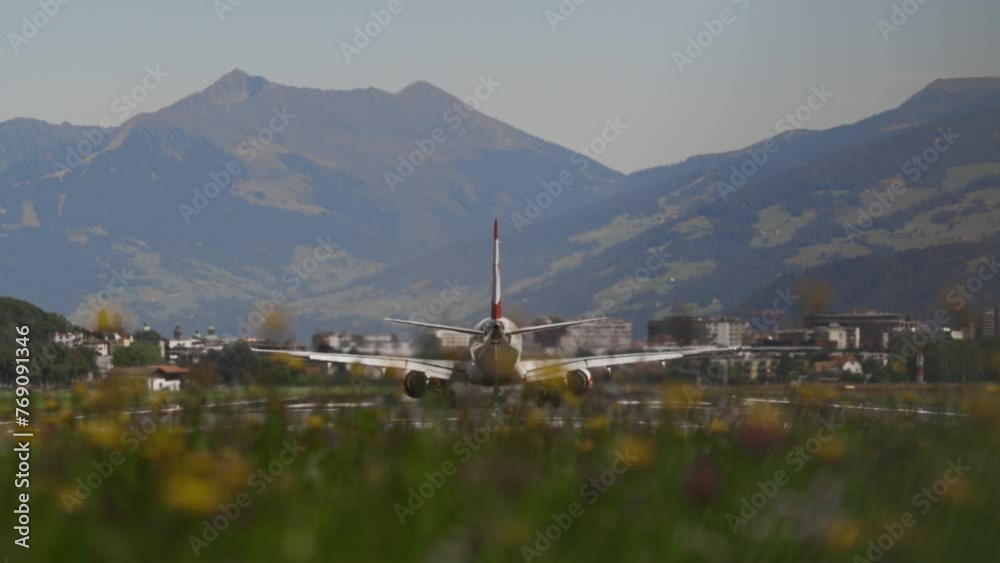 The plane picks up speed on the runway, takes off against the background of mountains and blurred yellow flowers