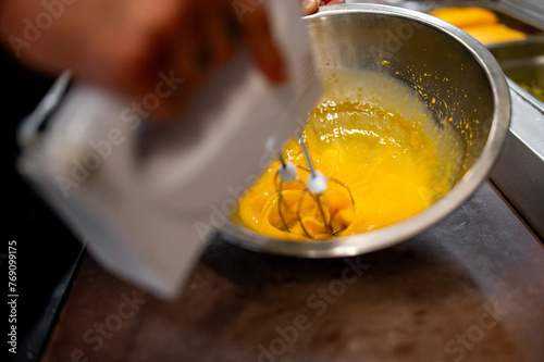 A person using an electric mixer to blend a yellow batter in a stainless steel bowl