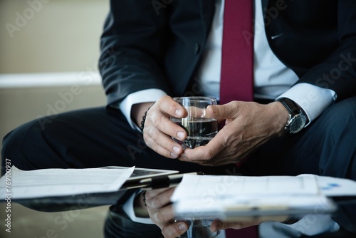 Close up of businessman in formal wear holding glass of fresh water while sitting in the modern office.