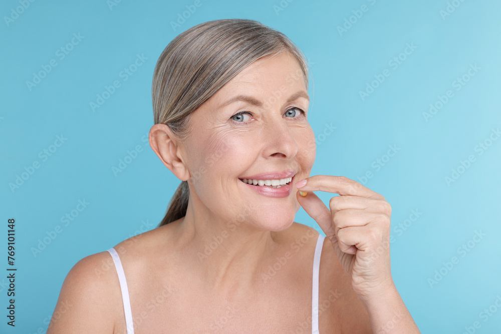 Beautiful woman taking vitamin pill on light blue background Beautiful woman taking vitamin pill on light blue background