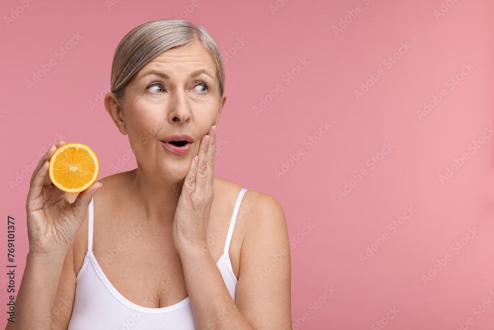 Beautiful woman with half of orange rich in vitamin C on pink background, space for text Beautiful woman with half of orange rich in vitamin C on pink background, space for text