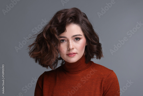 Portrait of beautiful young woman with wavy hairstyle on grey background