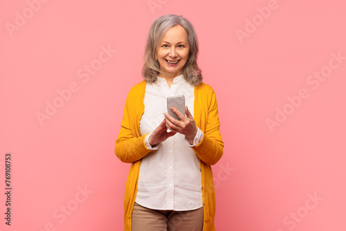 Cheerful mature gray haired woman texting via cell phone, studio