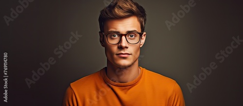 A man with a pair of glasses and an orange short-sleeved shirt makes eye contact with the camera photo