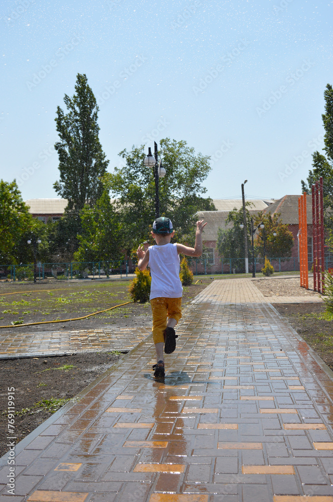 a boy runs through splashes of water on a hot summer day. freshness from cool water while walking in a city park. active lifestyle. children's joys and pranks