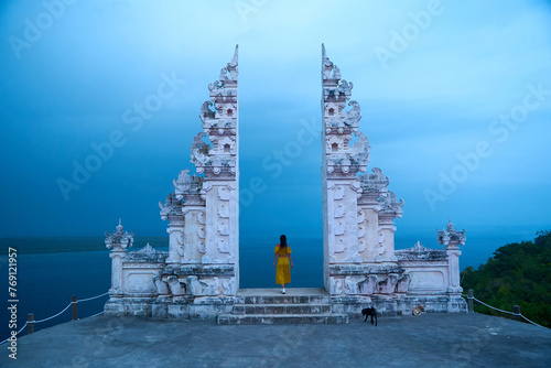 A woman in a yellow dress stands at a famous Balinese traditional gate on the island of Nusa Penida.
