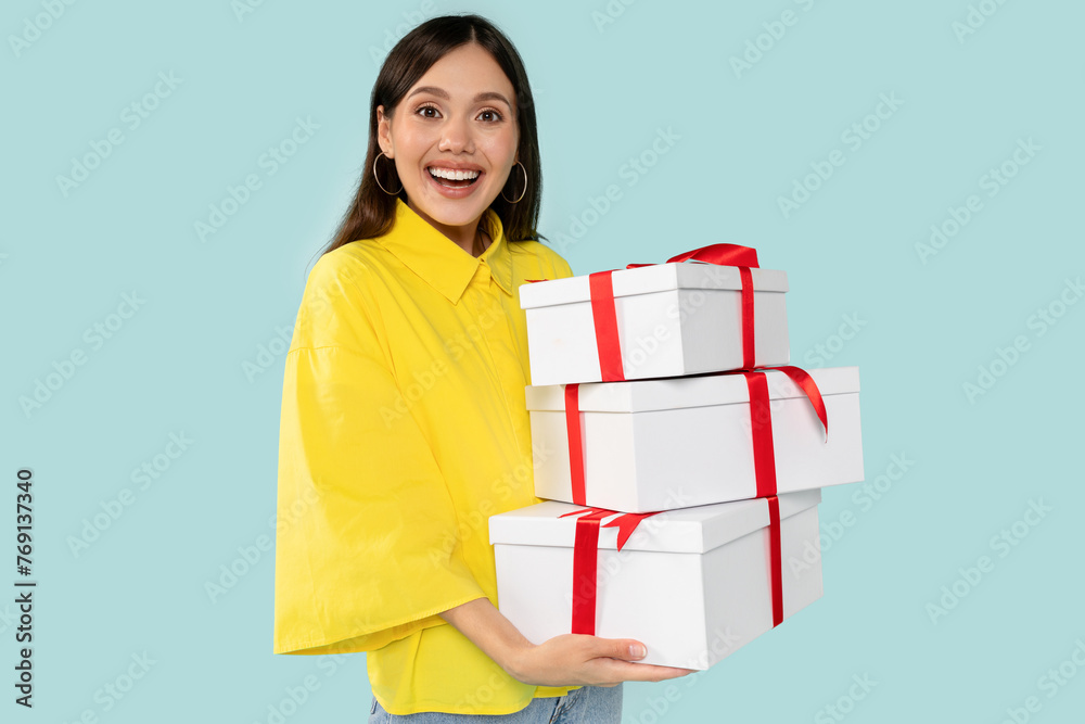 Excited young woman holding stylish white gifts with bold red ribbons at blue background Excited young woman holding stylish white gifts with bold red ribbons at blue background