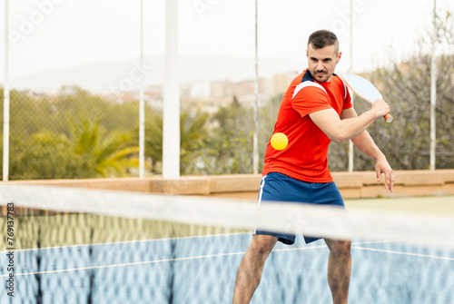 An adult man in sportswear is playing a game of pickleball on an outdoor court.The man is making a backhand with the racket to hit the ball.Pickle ball concept. Men Playing Pickleball photo