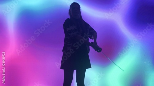 Person against big digital wall in studio. Woman silhouette with japanese sword katana acts in front of digital screen neon graphic visual background.