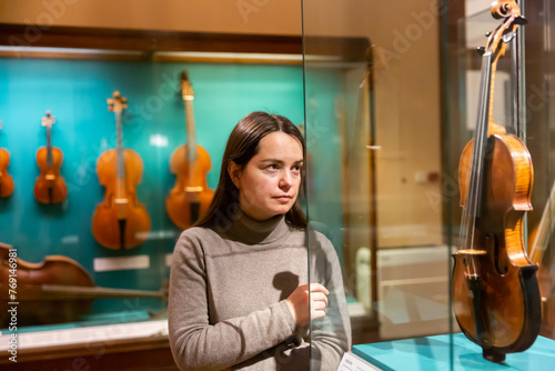 Female museum visitor examining with interest ancient stringed musical instruments displayed on exhibition .. photo