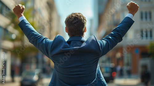 Back view of a happy businessman in a blue suit with raised arms celebrating success on a city street