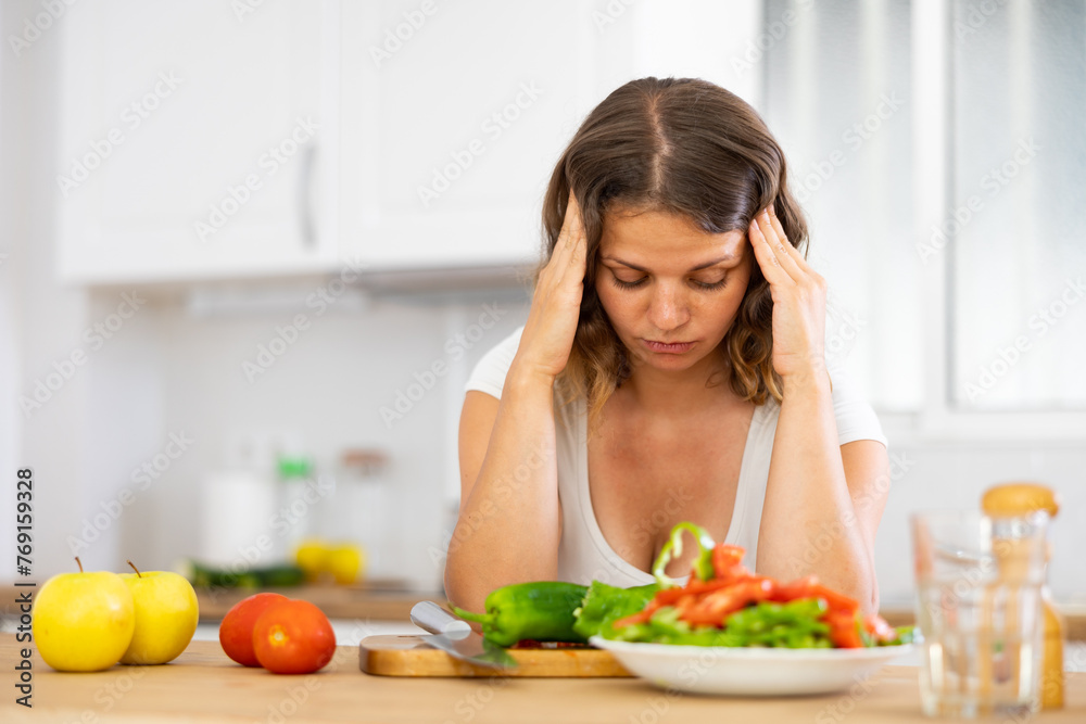 Portrait of thinking young woman during cutting vegetable on kitchen, looking with disgust and dislike