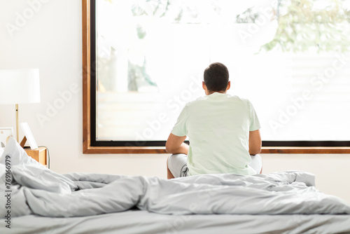 Man sitting on bed facing window