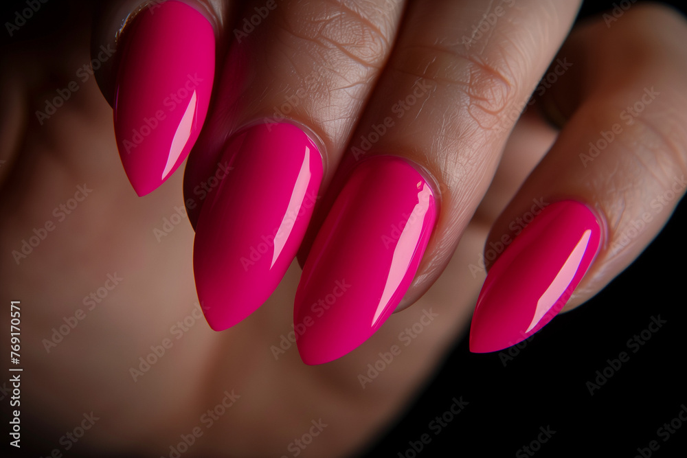 Close up of a woman's hand with a bright pink manicure against dark background Close up of a woman's hand with a bright pink manicure against dark background