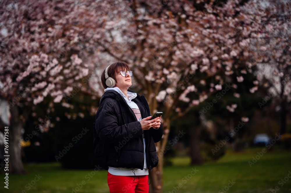 A woman with a contented smile enjoys the melody of her music amidst the delicate pink of cherry blossoms in a serene park setting A woman with a contented smile enjoys the melody of her music amidst the delicate pink of cherry blossoms in a serene park setting