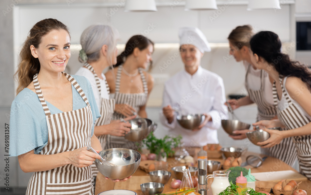 Young woman holding bowl in her hands posing surrounded by other members of cooking course
