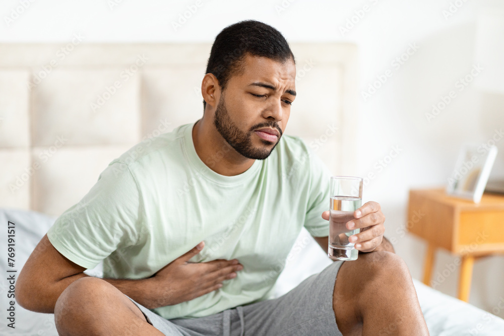 Man in bed holding stomach and glass