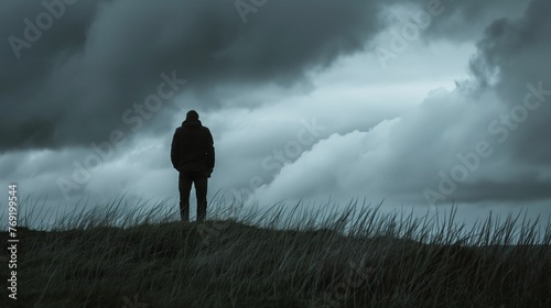 Image of lone figure under a sky heavy with dark clouds.