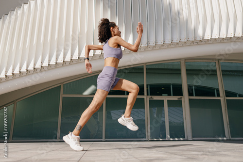 Active woman athlete is jogging on morning on modern building background. Healthy life concept