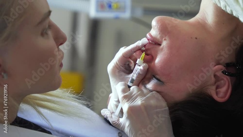 Vertical shot of Beautician doctor makes botox injection in the lips of young beautiful woman. Extreme close up 4k shot photo