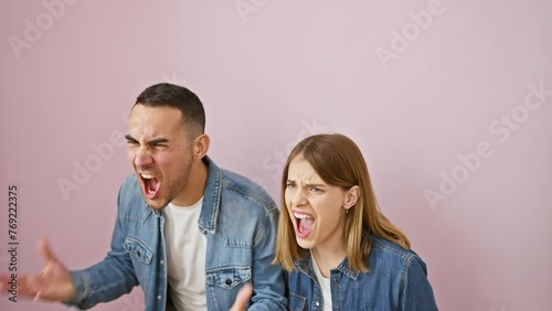 Frustrated beautiful couple in denim shirts stand furious, screaming and shouting in anger. mad rage overflows on isolated pink background photo