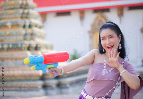 Portrait cheerful young asian woman holding plastic water gun Smiling and having fun playing in the water Songkran festival, Thailand. isolated on pink background. Thai New Year's Day.