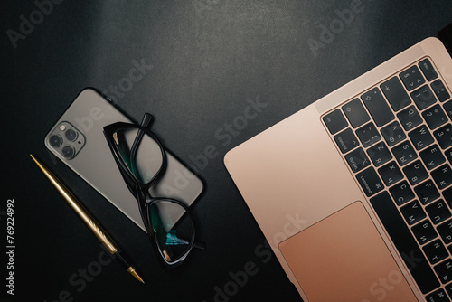 Business layout with items for design. Phone, glasses, pen, laptop on the table. In a dark style, there are object layouts on the table. Top view of items
