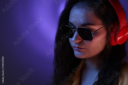 Portrait of beautiful young woman with headphones on color background with neon lights