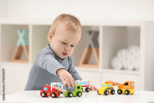 Children toys. Cute little boy playing with toy cars at white table in room, space for text