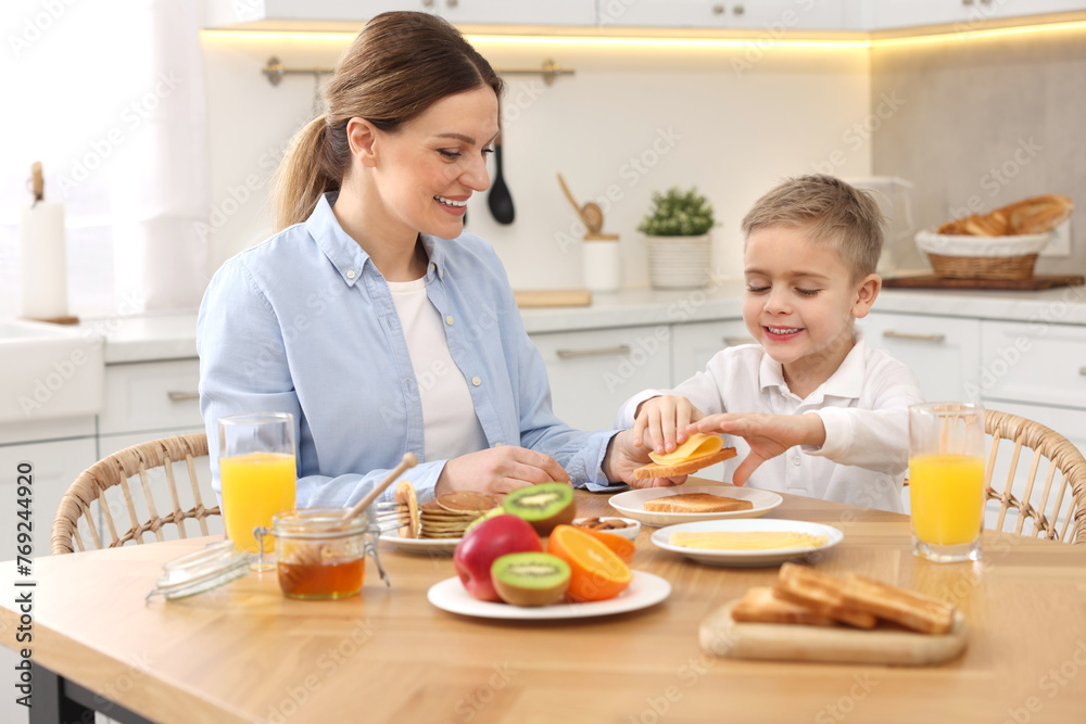 Mother and her cute little son having breakfast at table in kitchen