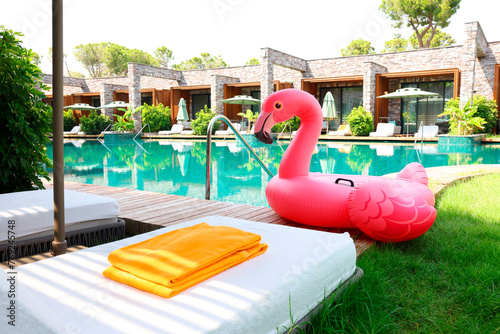 Fototapeta Naklejka Na Ścianę i Meble -  Float in shape of flamingo on wooden deck near swimming pool and sunbeds at luxury resort
