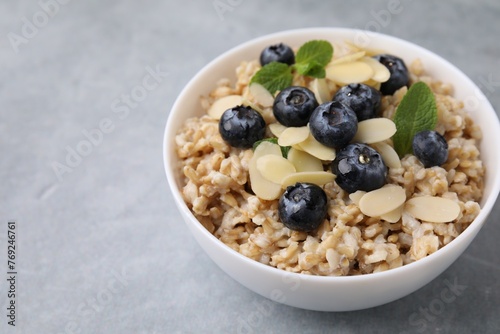 Tasty oatmeal with blueberries, mint and almond petals in bowl on grey table. Space for text