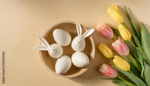 easter concept top view photo of white circle easter eggs in wooden holder ceramic bunnies yellow and pink tulips on isolated pastel beige background with copyspace