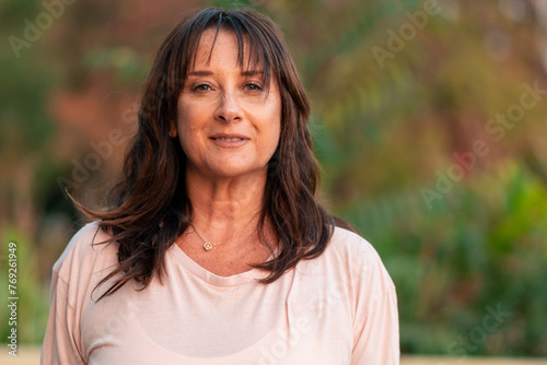 Beautiful senior woman 50 to 60 years old posing in casual clothes, smiling in an outdoor park at sunset photo