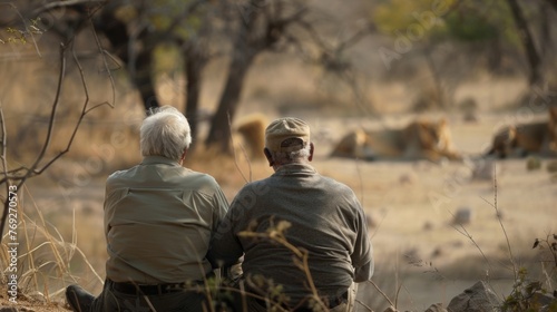 An elderly couple backs to the camera clutch each others hands tightly as they watch a pride of lions lazing in the shade a . . photo