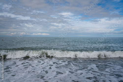 Fototapeta Naklejka Na Ścianę i Meble -  An incoming wave on the Black Sea and a pebble beach on the Sochi coast on a sunny summer day with clouds, Sochi, Krasnodar Territory, Russia