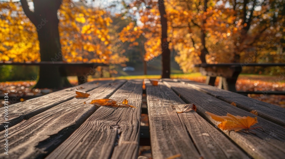 Close-up of a wooden table in a park covered with leaves, showcasing natures presence in an urban setting. - obrazy, fototapety, plakaty 