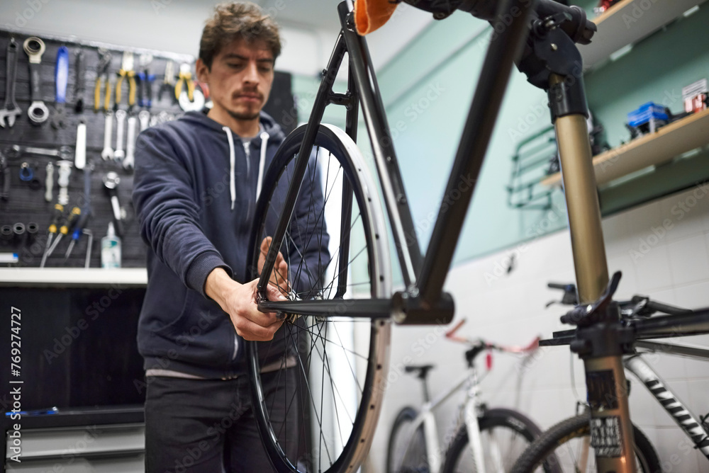 Hispanic man evaluating the alignment of the rear wheel of a bicycle he is servicing in his workshop. Real people at work. Hispanic man evaluating the alignment of the rear wheel of a bicycle he is servicing in his workshop. Real people at work.
