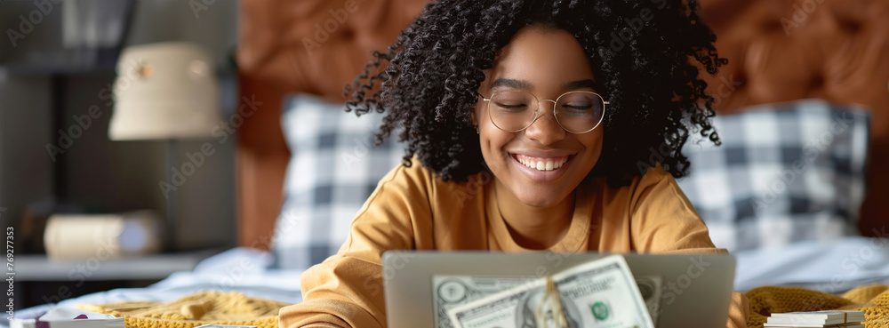A person joyfully checking their investment portfolio, celebrating achieving financial independence with a laptop and a stack of money. - obrazy, fototapety, plakaty 