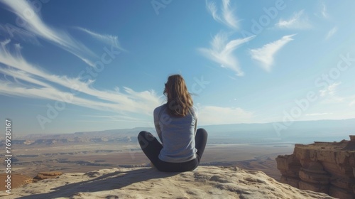 A woman sits crosslegged on a rock back to the camera as gazes towards the endless blue sky and endless stretch of the desert . . © Justlight
