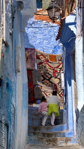 Two children climbing stairs in front of a colorful rug in the medina in Chefchaouen, Morocco © Angela