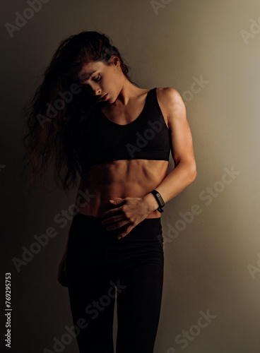 Sport muscular woman relaxing after training in black sport bra looking on strong abs on dark shadow studio background. Sexy body. Sporty art toned